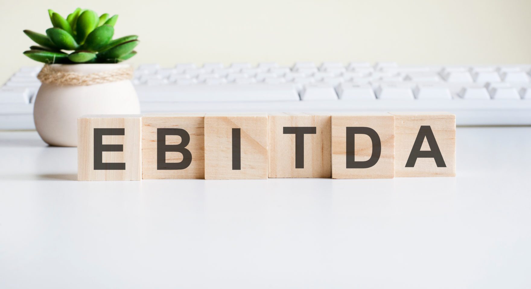 ebitda word made with wooden blocks. front view concepts, green plant in a flower vase and white keyboard on background