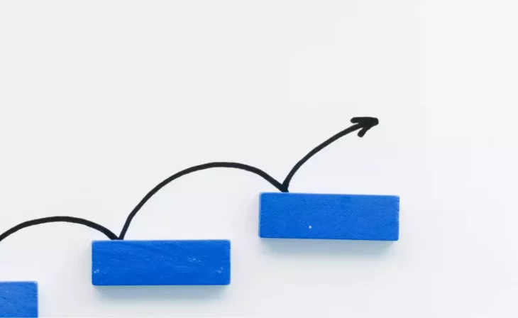 Blue blocks stepping upwards with a drawn arrow indicating progress on a white background.