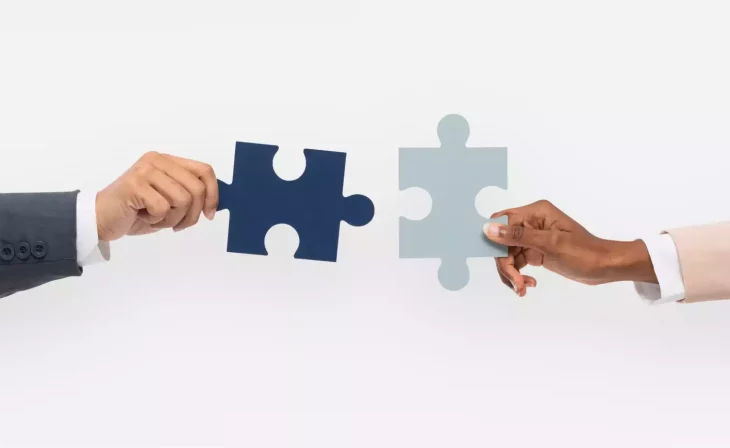 Two hands from diverse individuals holding matching puzzle pieces, poised to connect.