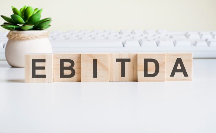 ebitda word made with wooden blocks. front view concepts, green plant in a flower vase and white keyboard on background